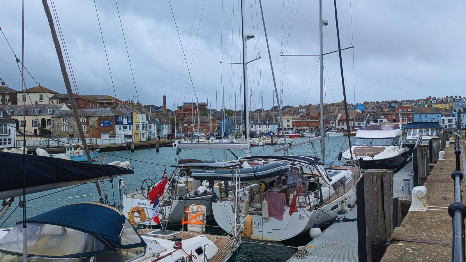 Yachts and a motor cruiser moored along a pontoon in a harbour town.