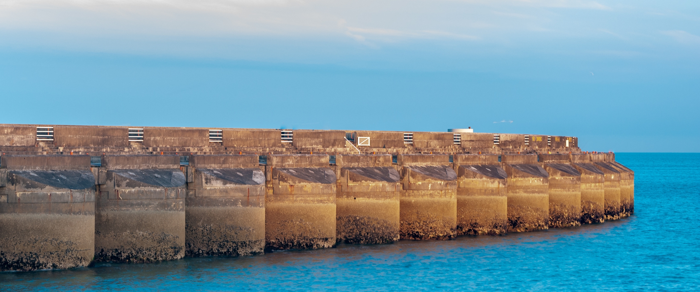 A long concrete breakwater extending into calm blue water.
